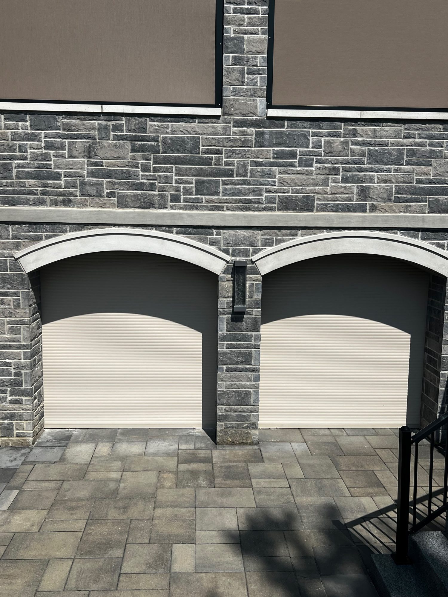 Two cream roll-up garage doors partly closed inside arched openings on a grey stone facade