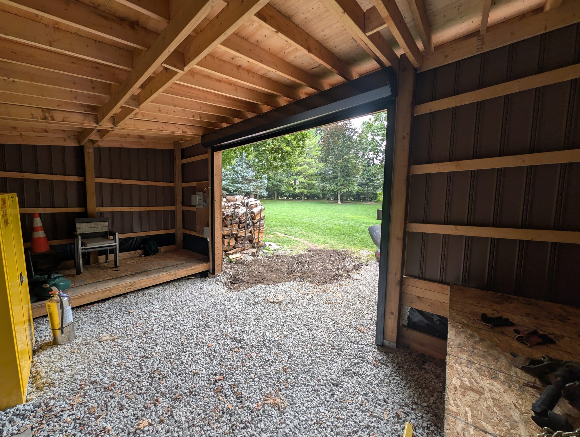 Interior of a timber-framed shed with a black roll-up door open to a lawn