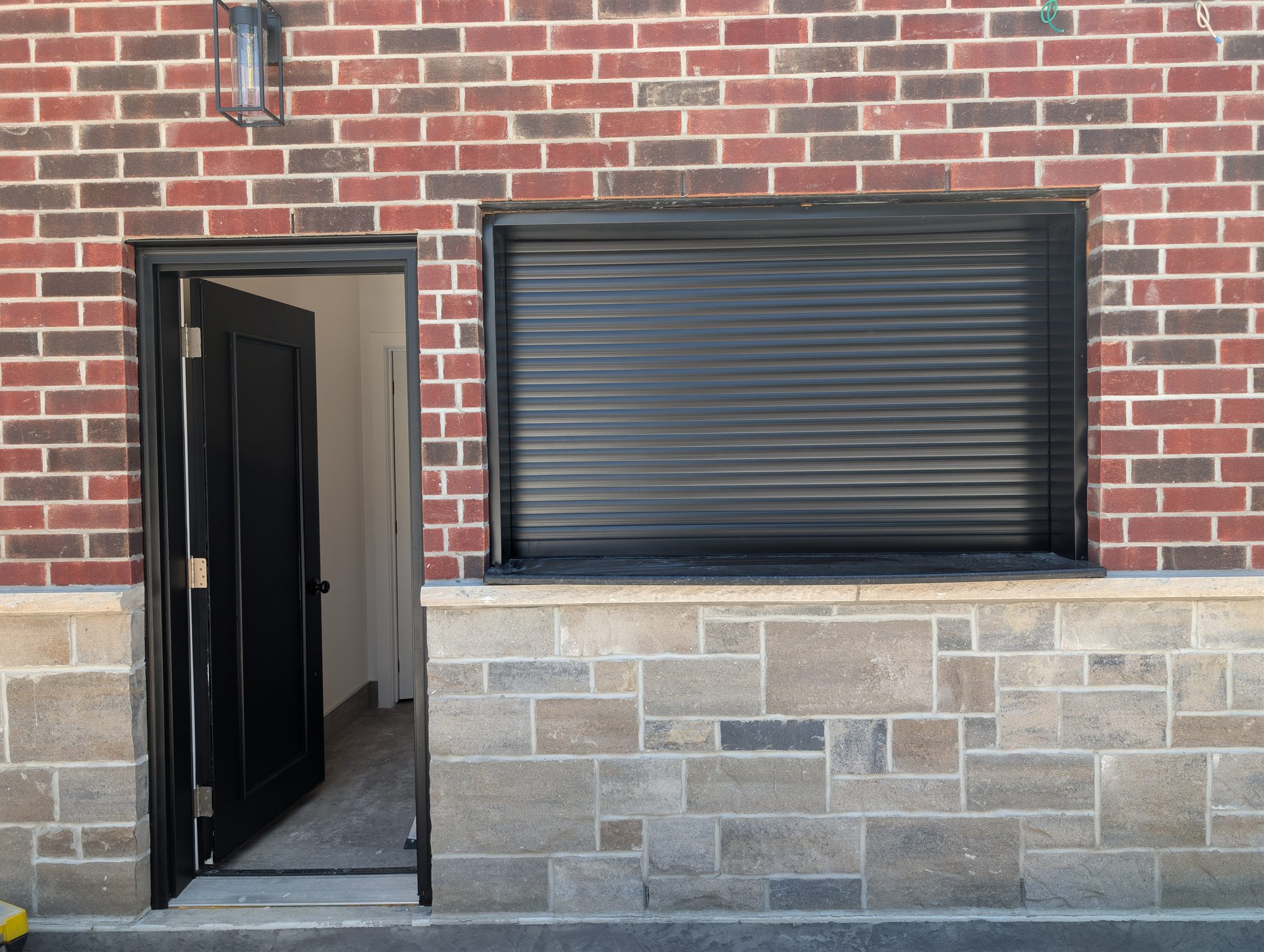 Black roll shutter closed over a wide servery opening in a brick and stone pool house exterior