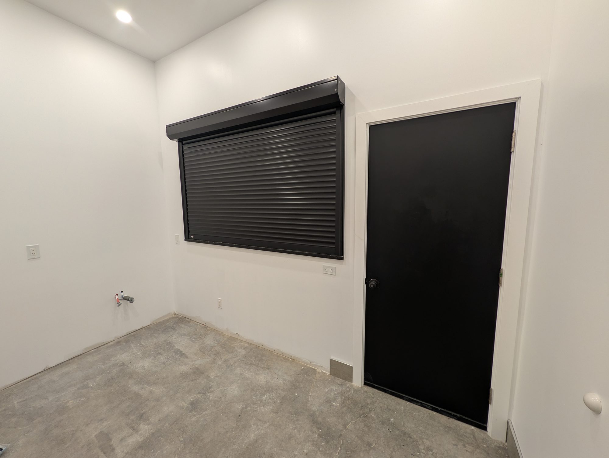 Black roll shutter closed over an interior servery opening in an unfinished pool house