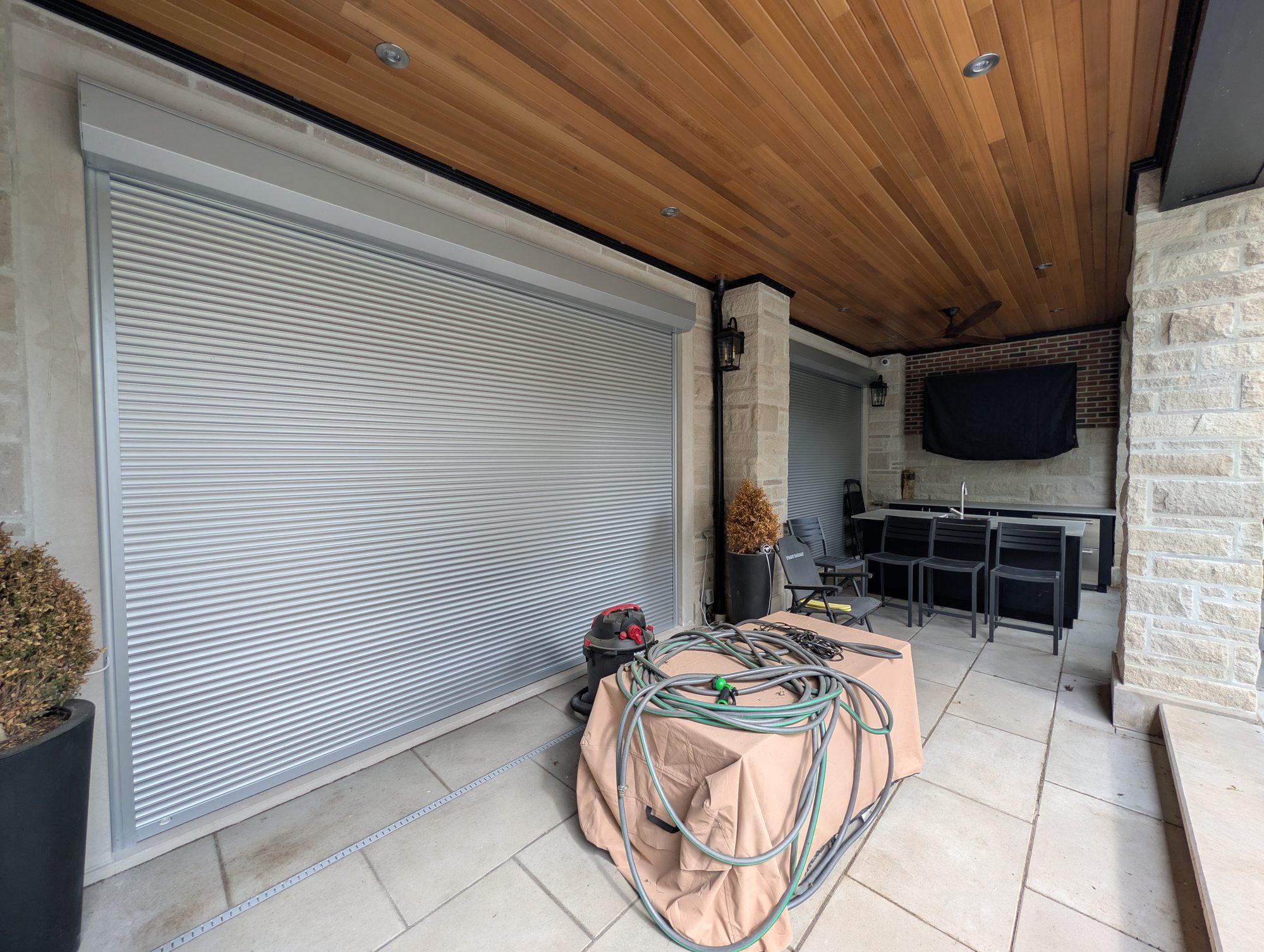 Grey roll shutter closed across a covered patio opening with an outdoor bar and cedar ceiling