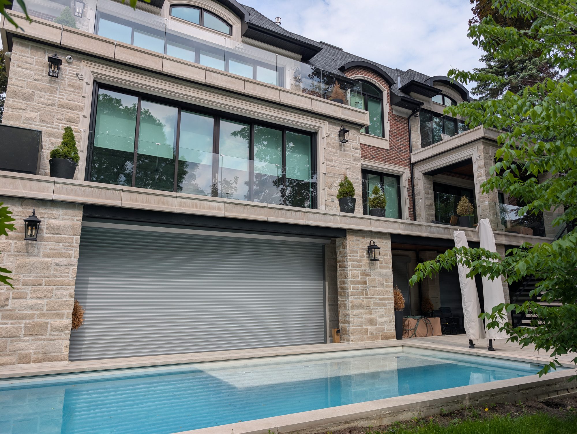 Grey roll shutter closed over a wide poolside opening on a large stone home