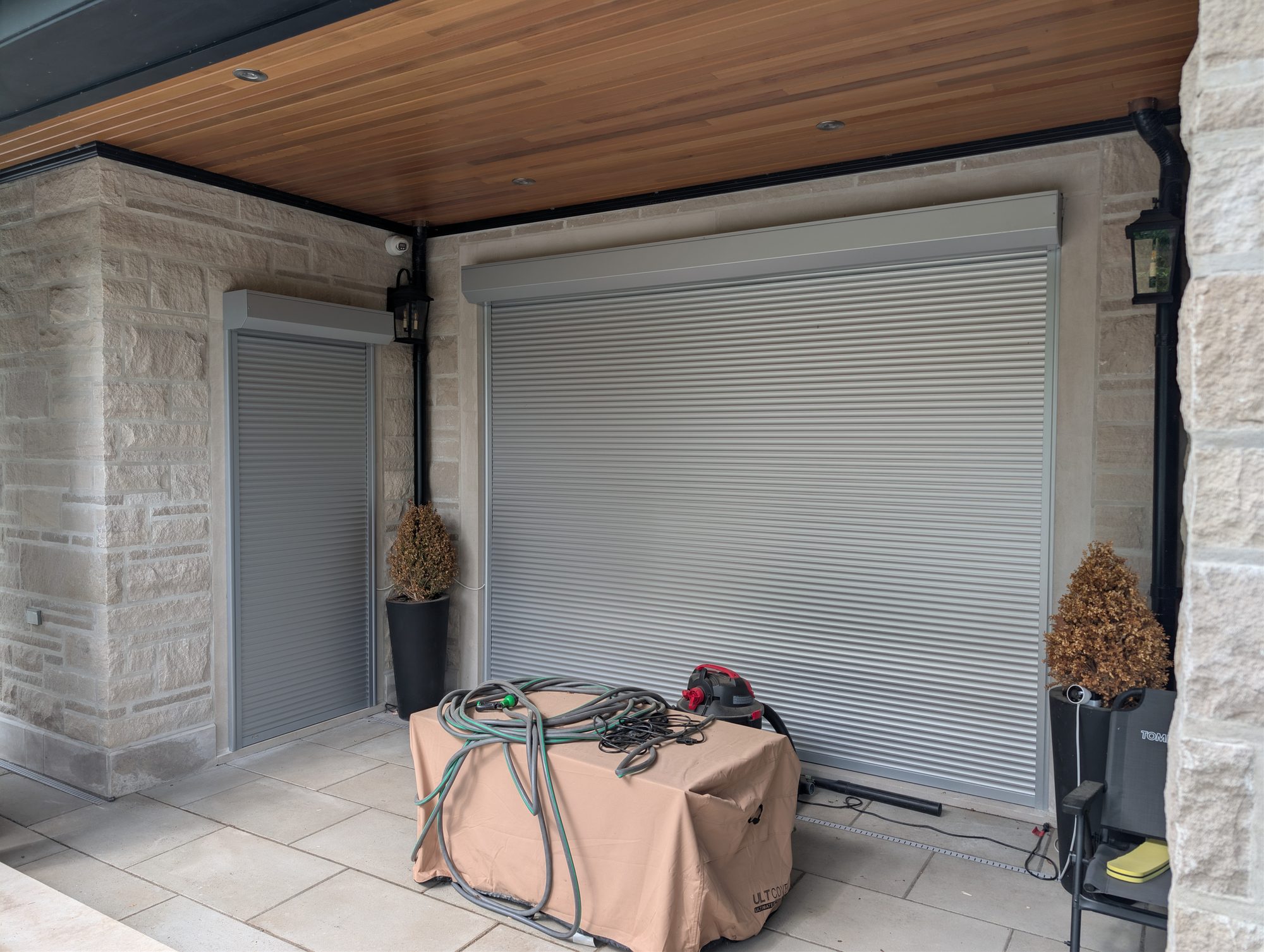 Roll shutters closed over a covered patio opening and side door between stone columns