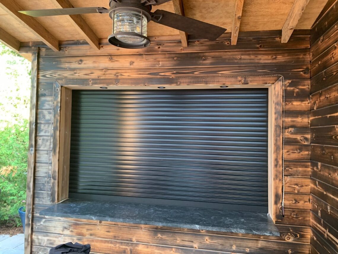 Dark-coloured roll-up shutter enclosing a backyard cabana at dusk