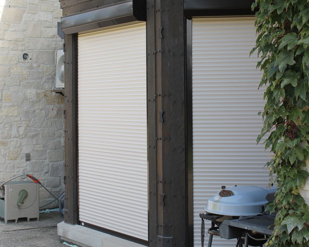 Two white roll-up shutters on a cabana with outdoor furniture