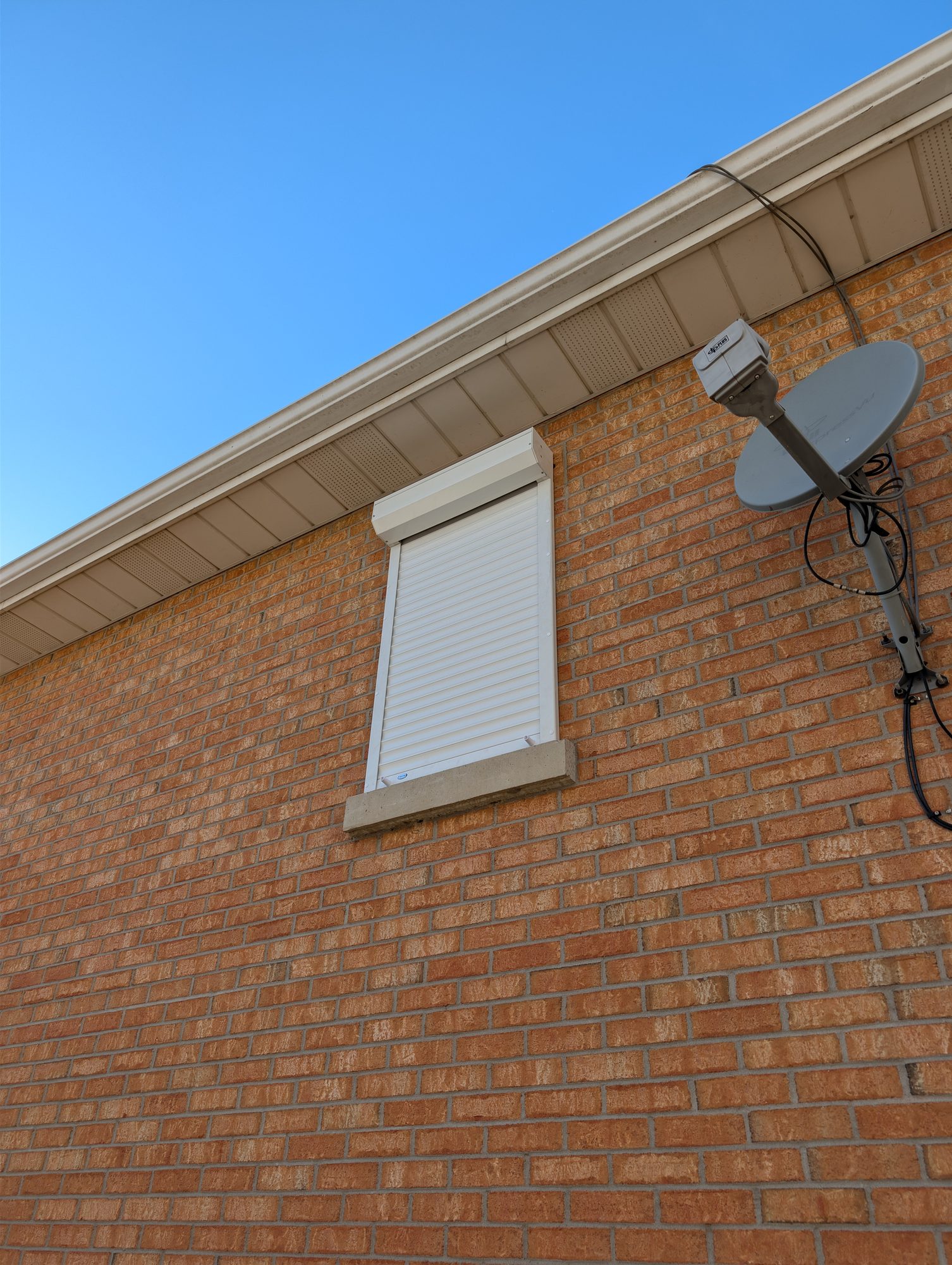 Close view of a white roll shutter closed over a single window on a brick wall
