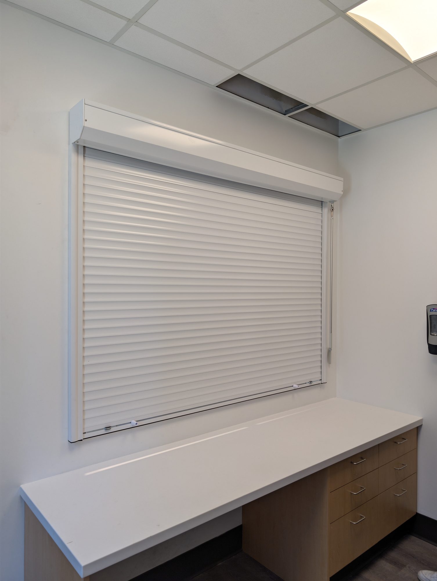 White roll-up counter shutter closed over an interior reception window above a office countertop