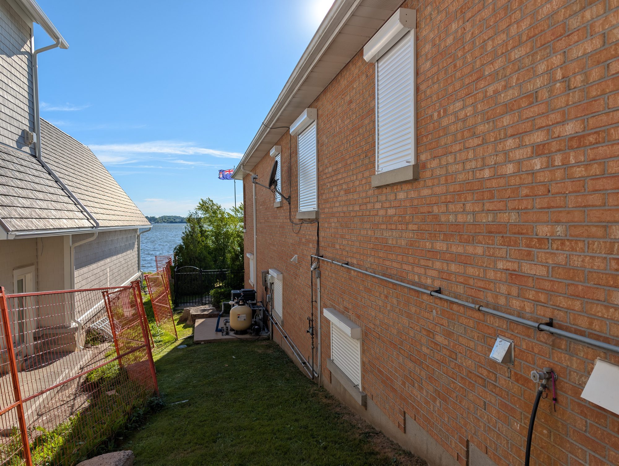 Row of white window roll shutters on the brick side elevation of a waterfront home