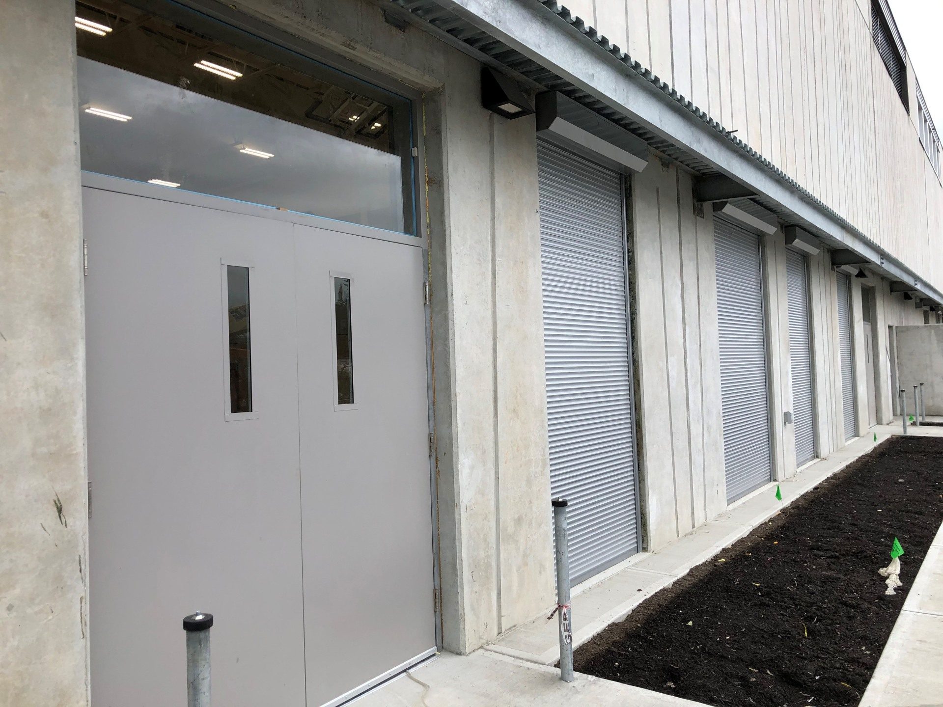 Grey roll shutters closed over narrow windows on a concrete institutional elevation beside a service door