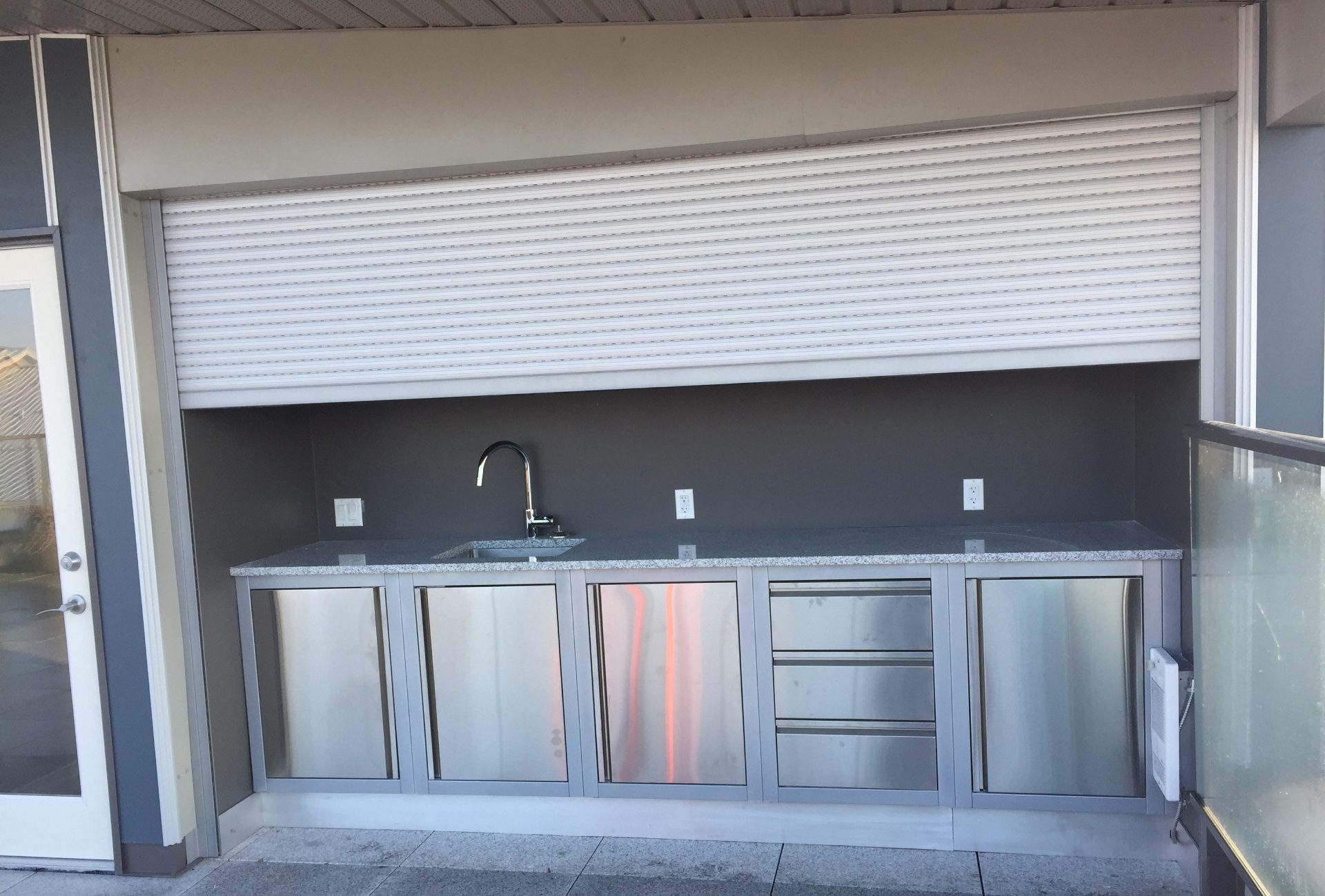 White roll shutter partly closed over an outdoor servery counter with a stainless steel base and sink