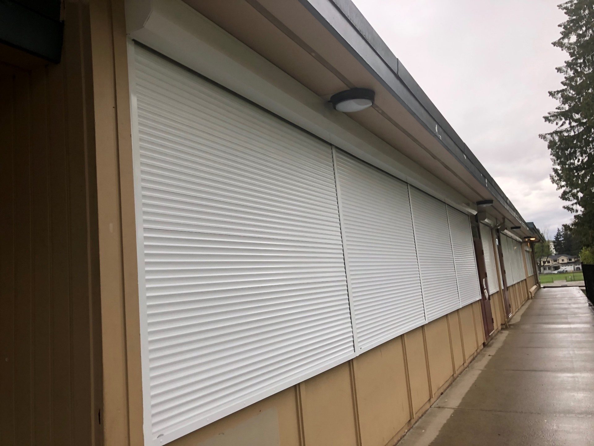 White roll shutters closed across a long classroom window band on a single-storey school