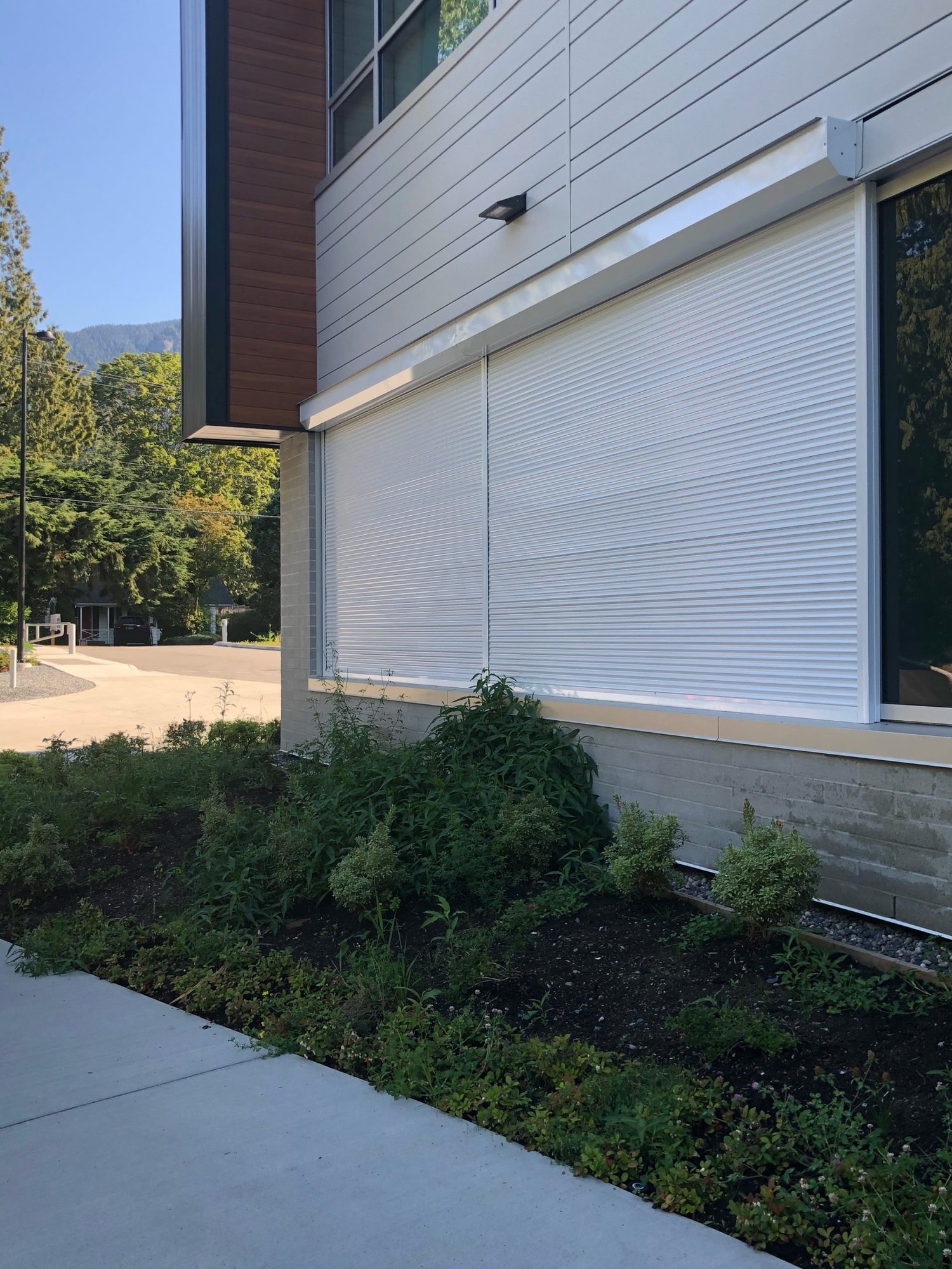 White roll shutters closed across a ground-floor classroom window band on a modern school building