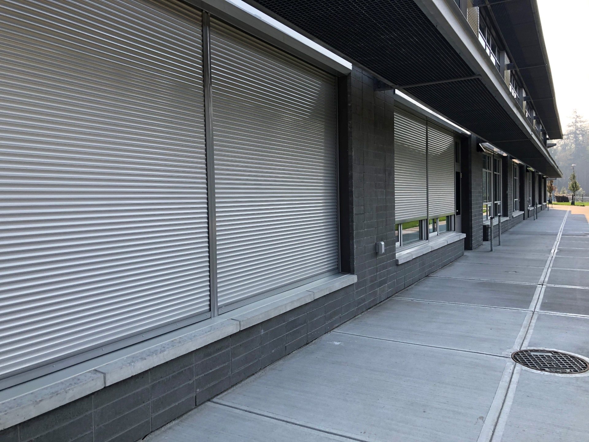 Run of grey roll shutters closed along a covered school walkway on a dark block elevation