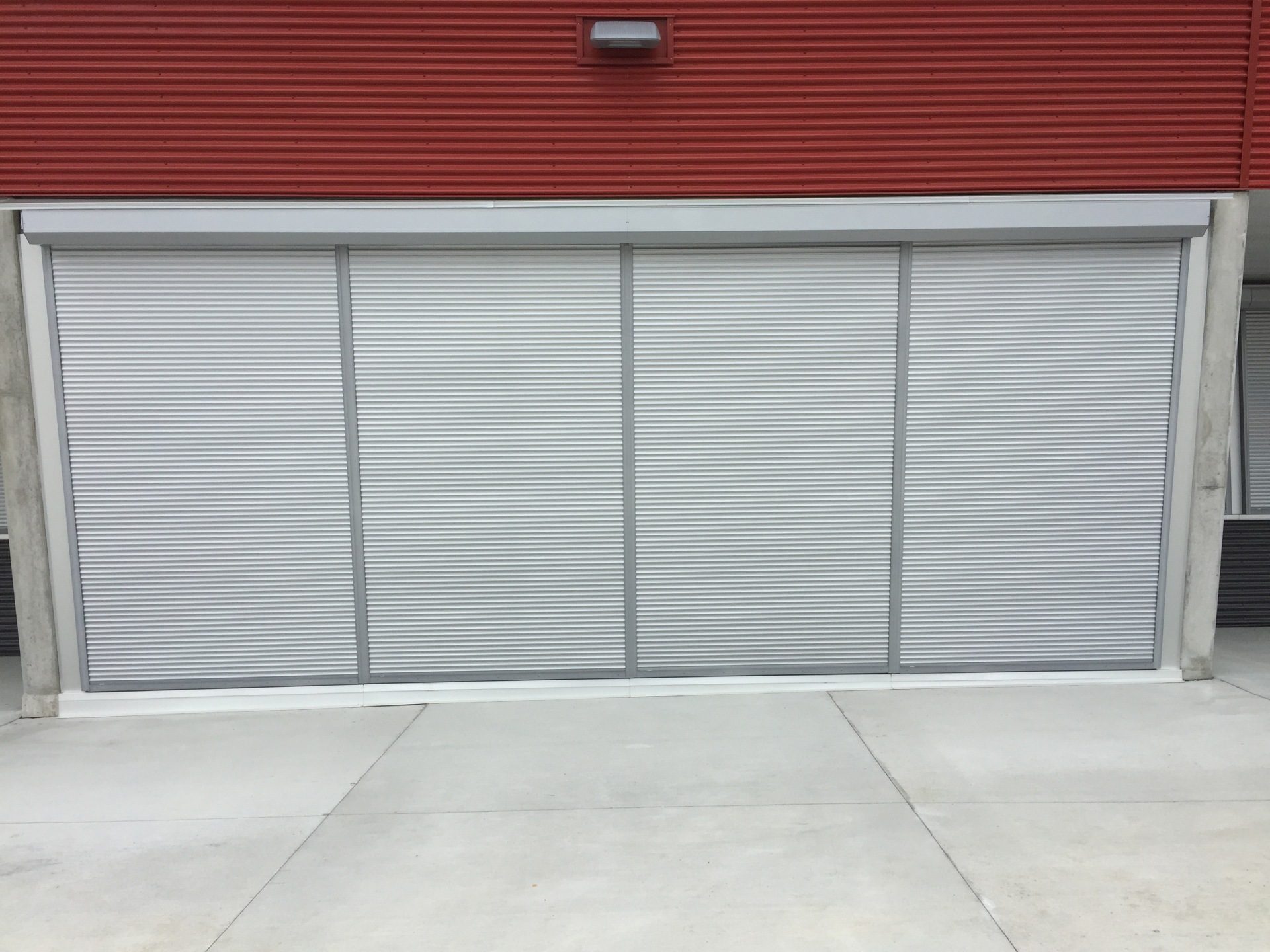 Four-panel bank of silver roll shutters closed across a wide opening on a red-clad building