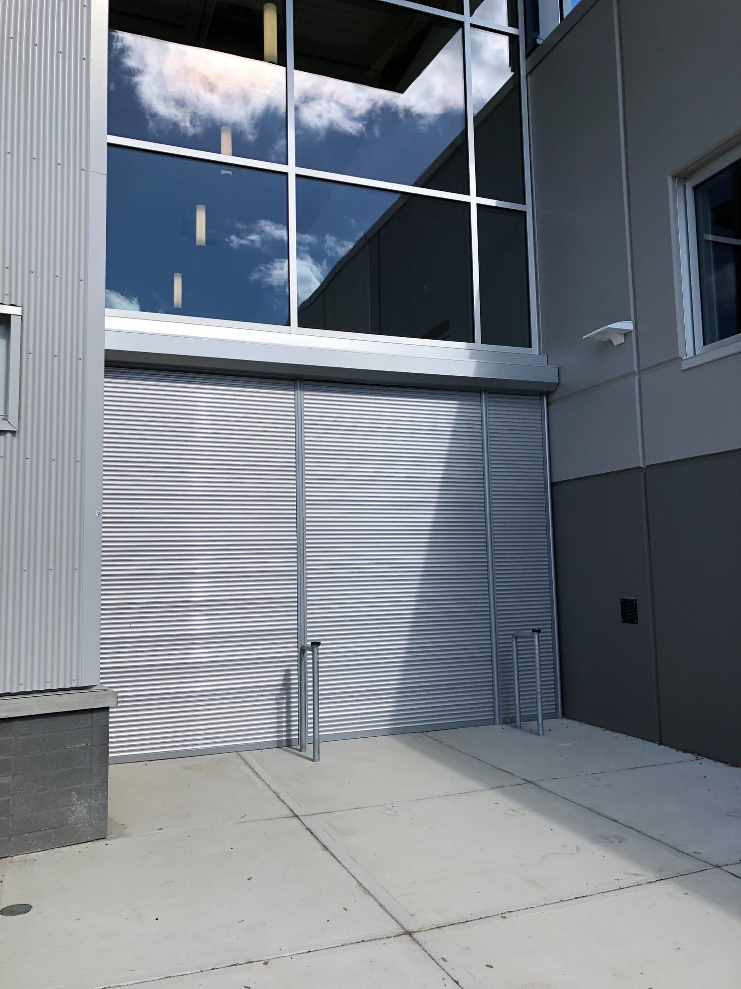 Wide grey roll shutter closed across a recessed building entrance beside curtain wall glazing