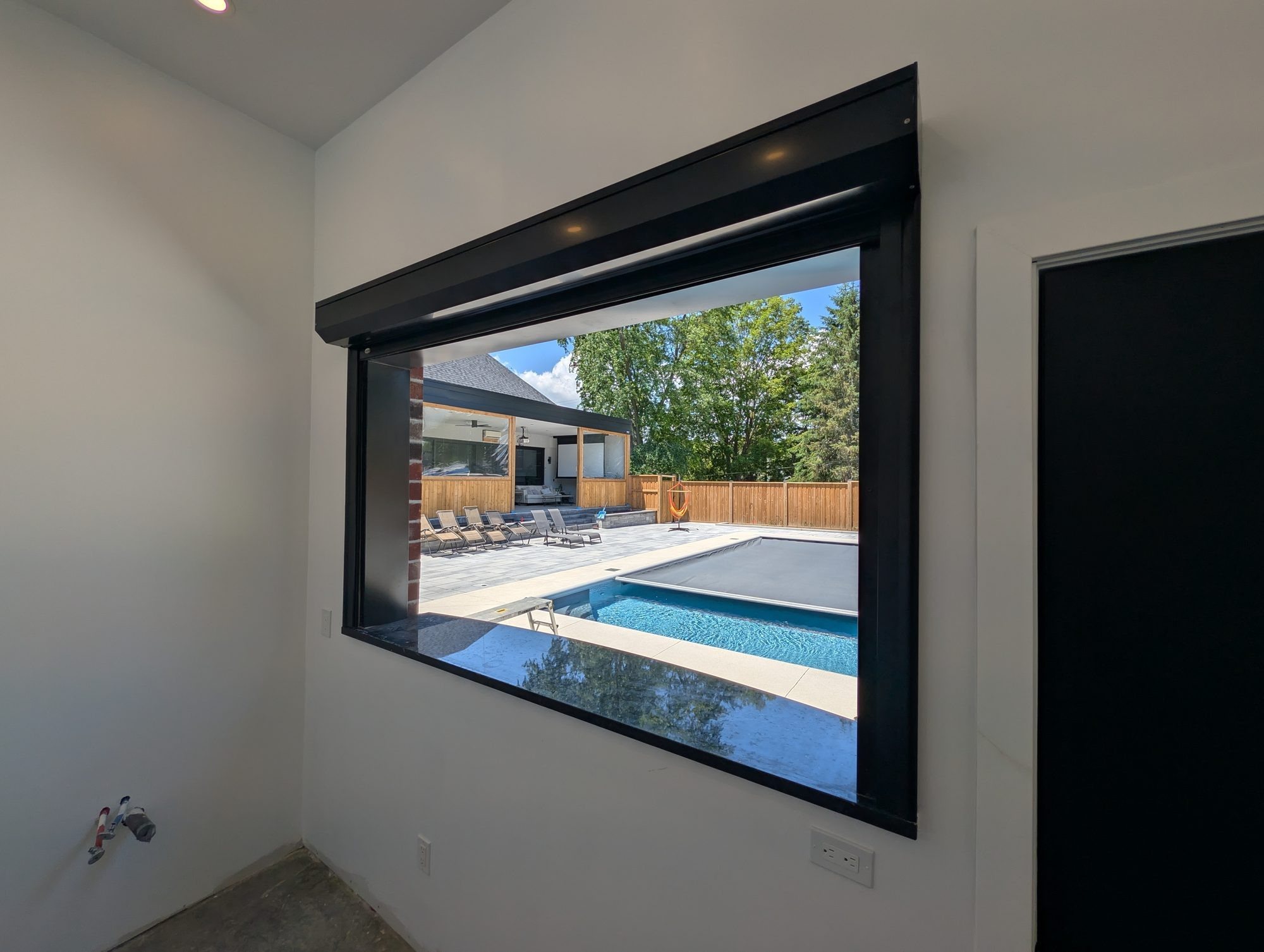 Black roll shutter raised above a pool house servery opening looking out to the pool