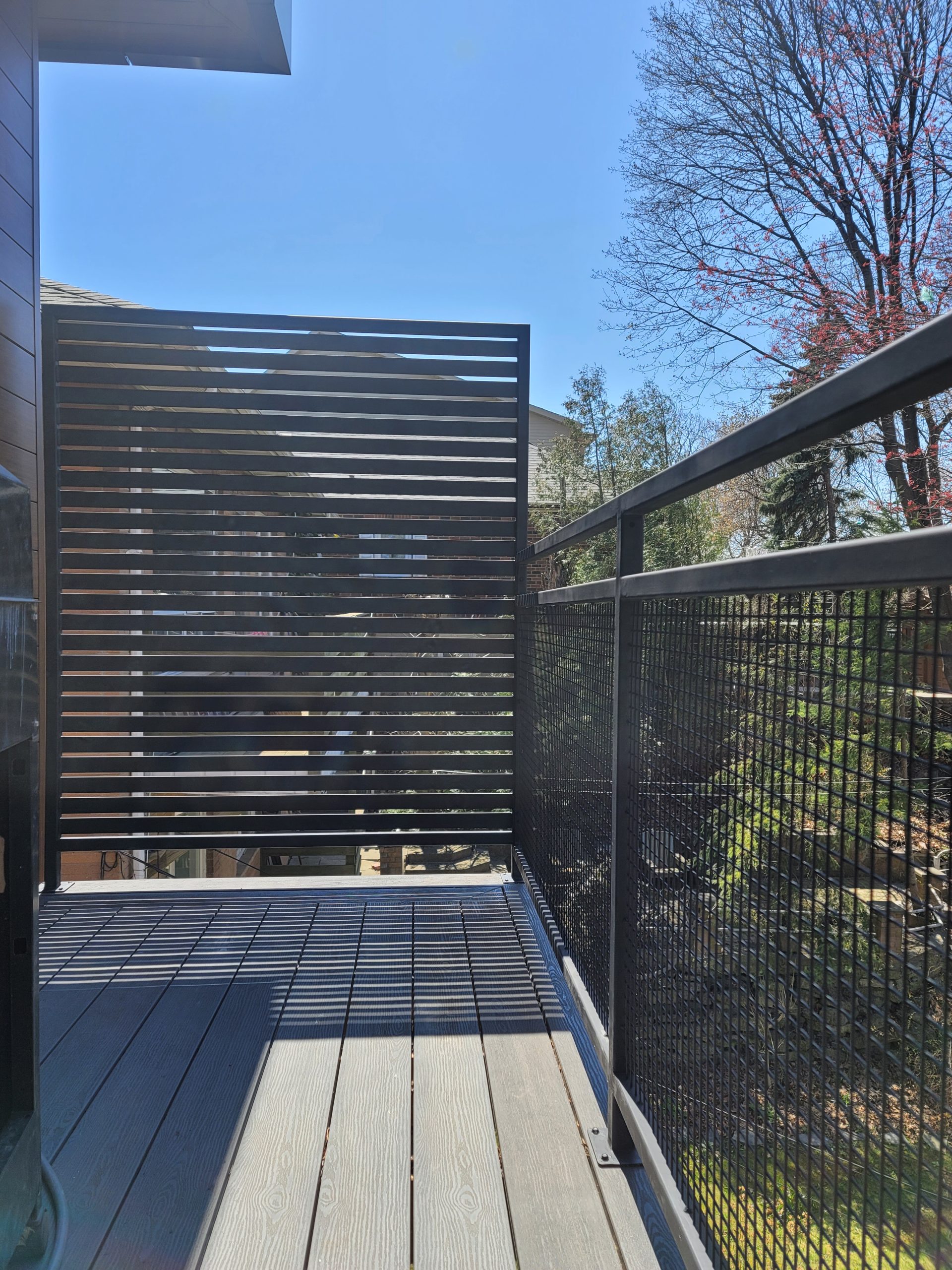 Black-framed horizontal slat privacy screen creating separation beside an exterior deck