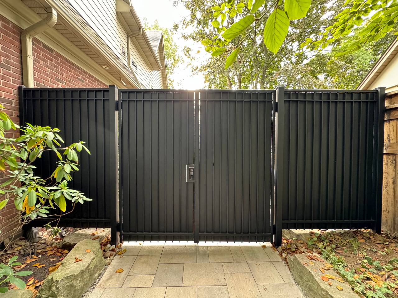 Black metal security gate with vertical pickets opening into a residential yard