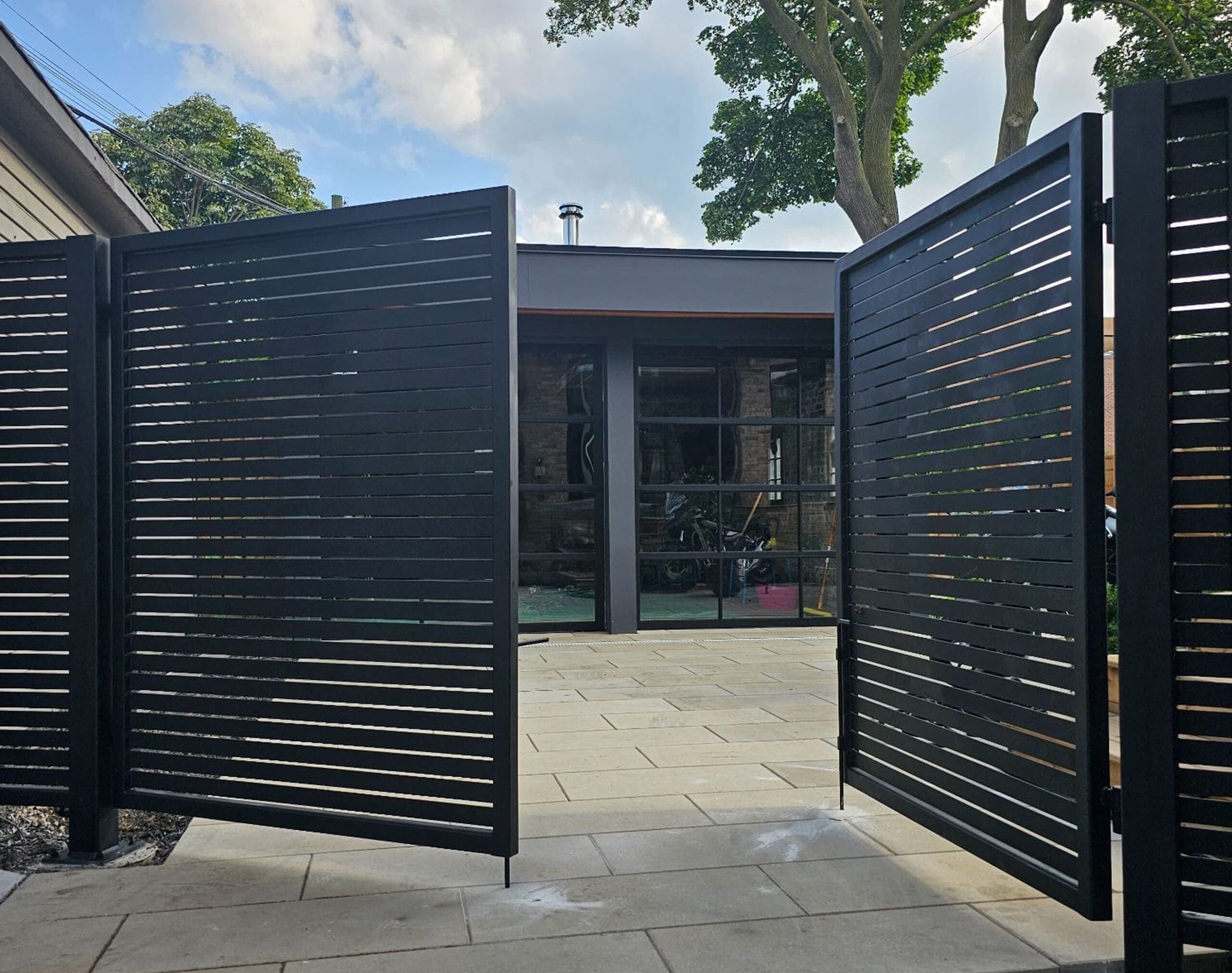 Modern black slatted swing gate opening into a private courtyard